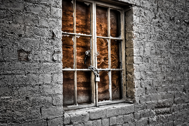A broken window that is padlocked with a chain.