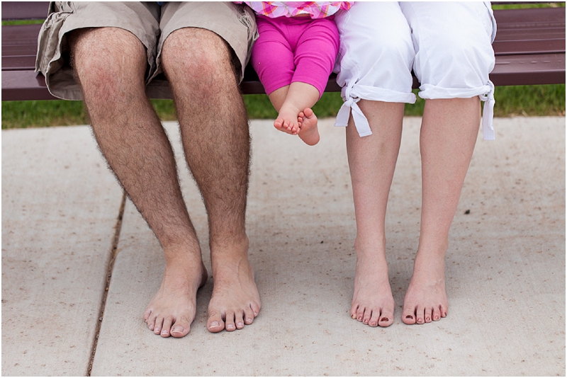 A young family sitting at a park bench showing their feet. 