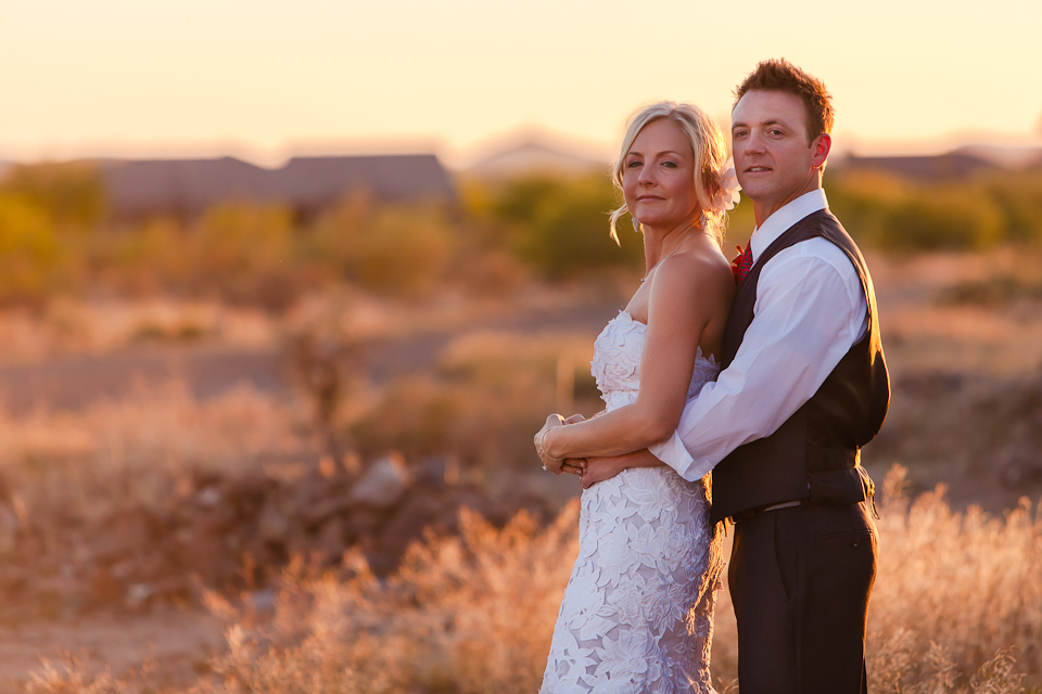 A bride and groom posing in the desert at sunset.