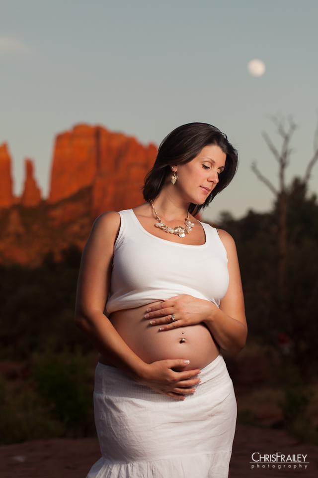 An expectant mother poses in front of the red rocks of Sedona and a full moon.