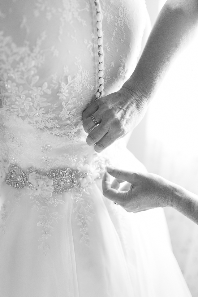 Mother of bride buttoning up bride's wedding dress.