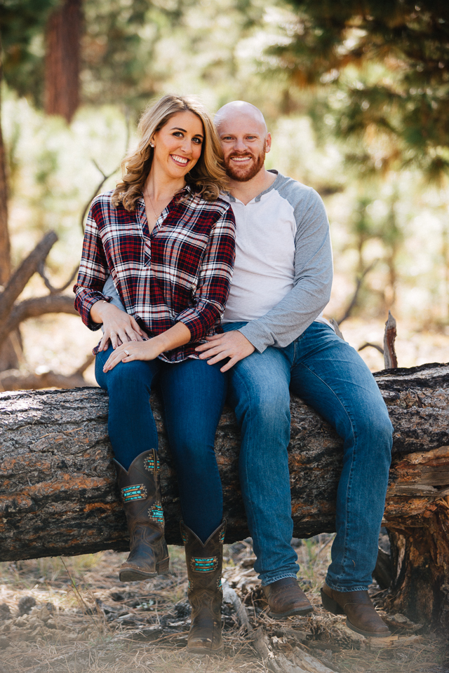 Couple sitting on a log posing in the woods.