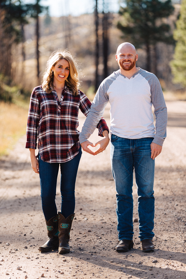 Couple standing on a dirt road making a heart shape with their hands. 