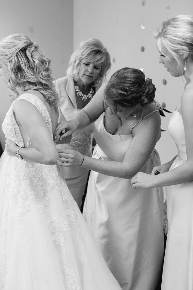 Bride getting buttoned up with help from her sisters. 
