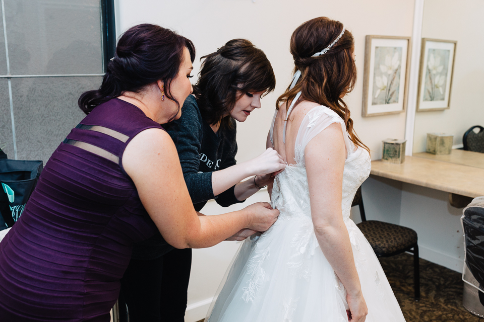 Mother and bridesmaid helping bride get into her wedding dress. 