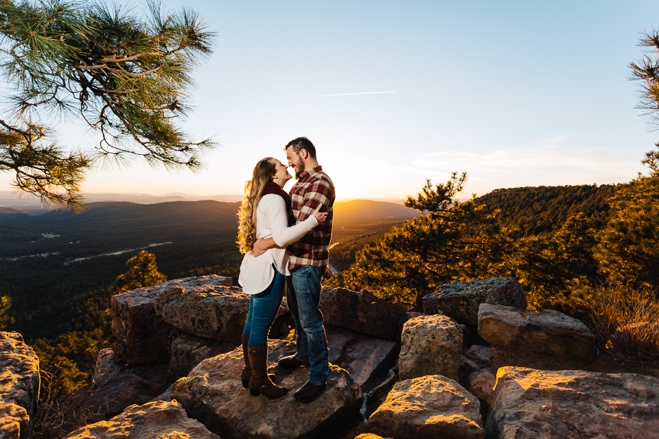 An engaged couple stands at the edge of the Mogollon Rim at sunset. 