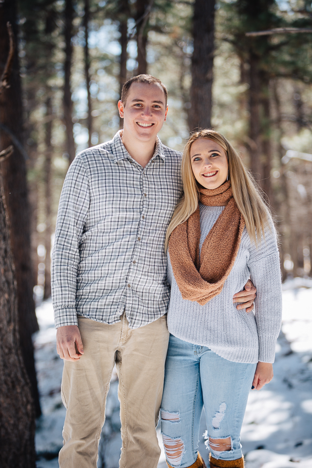 Couple posing in the woods with snow on the ground for their Flagstaff engagement session. 