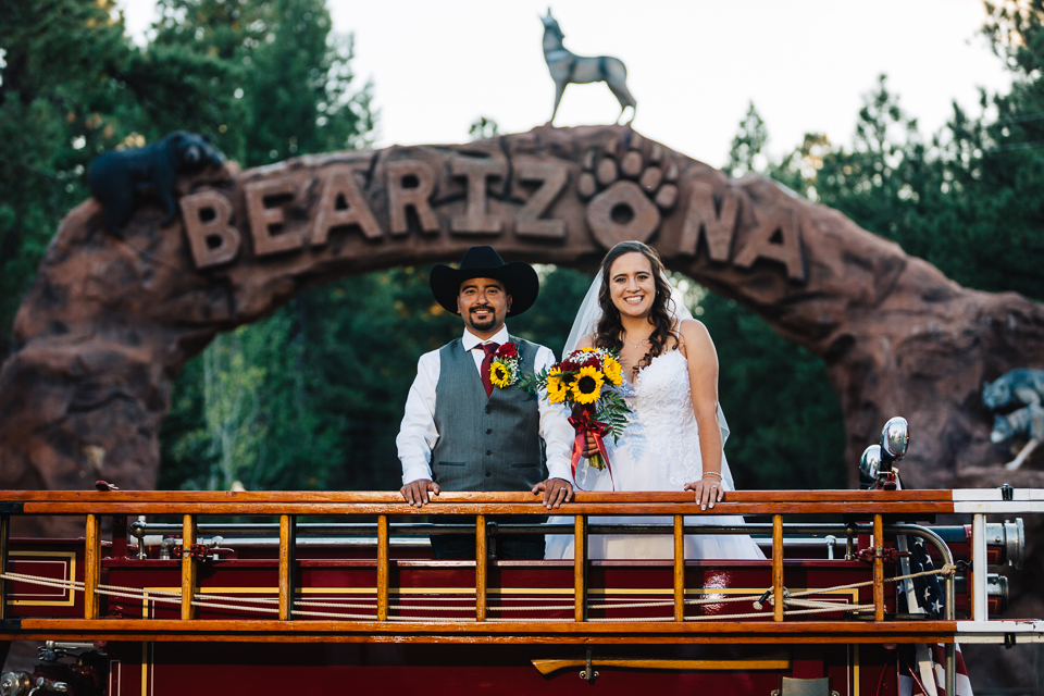 Bride and groom standing in back of firetruck in front of Bearizona sign.