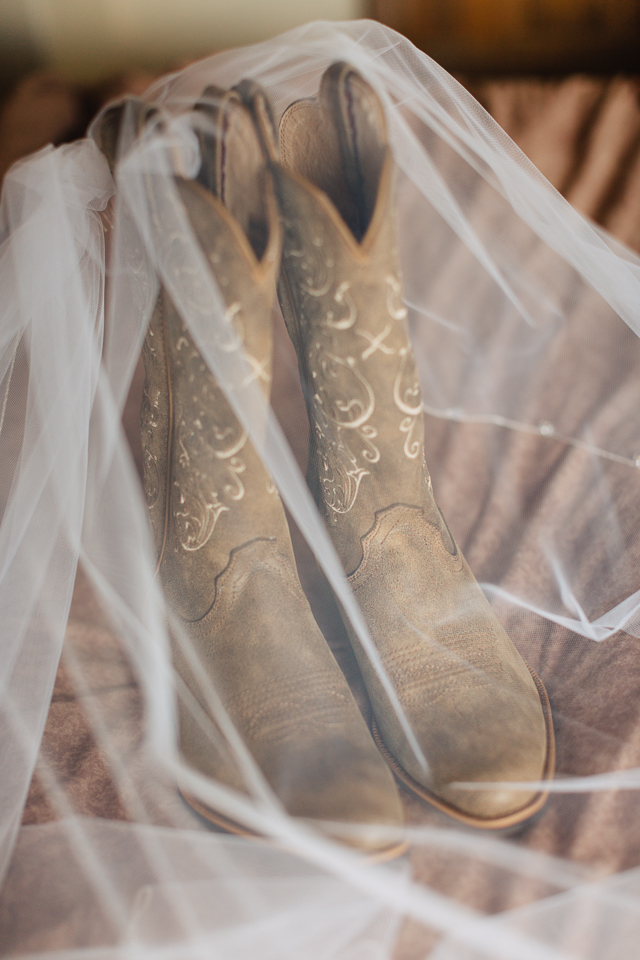 Bride's wedding veil draped over her cowboy boots. 