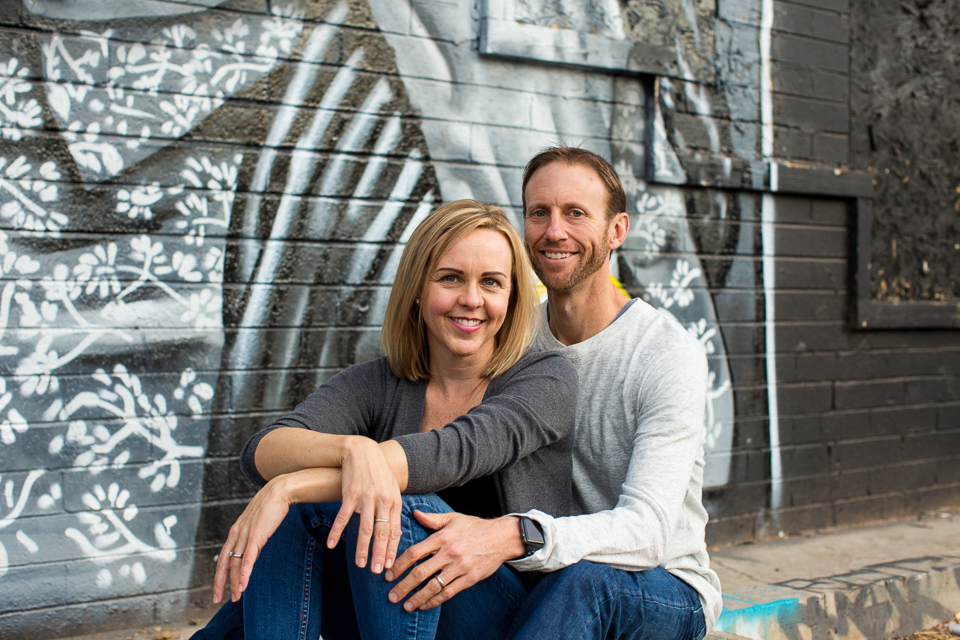 Husband and wife sitting in front of a graffiti wall. 