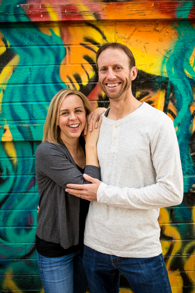 Husband and wife posing against graffiti wall. 