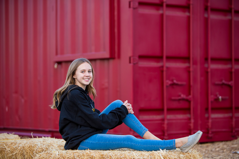Teenage girl sitting on hay bale for family photos.