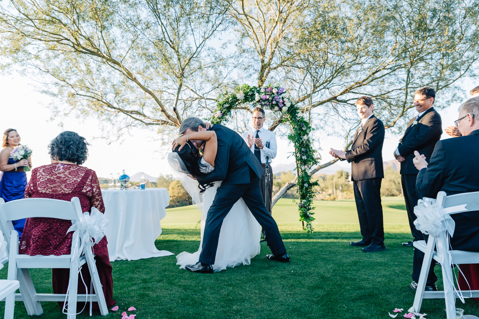 Groom dipping and kissing bride during wedding ceremony. 