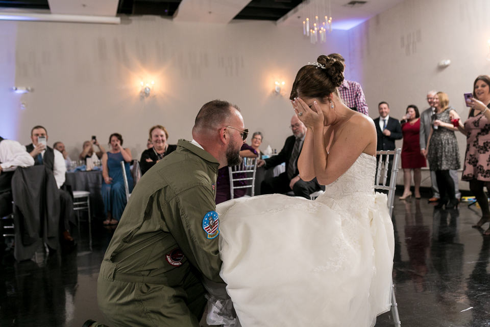 Groom dressed as Top Gun pilot taking off bride's garter. 