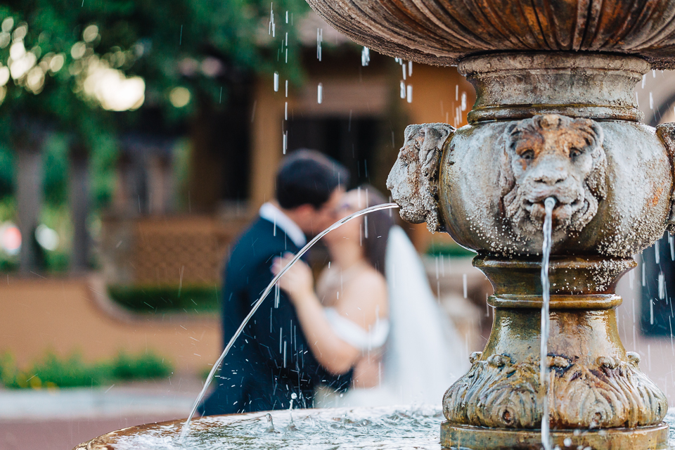 Bride and groom kissing behind a water fountain at Villa Siena. 