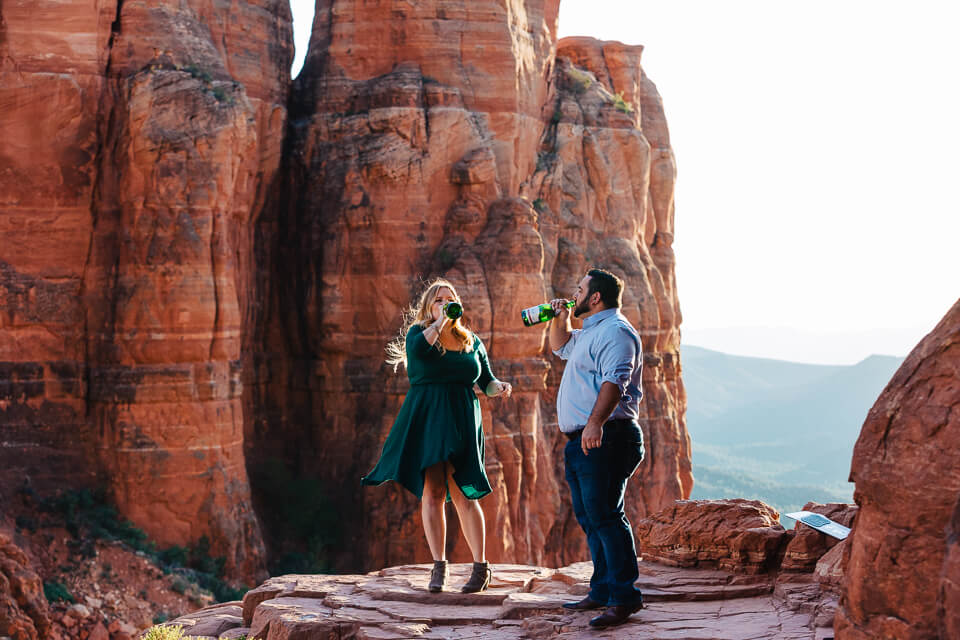 Engaged couple celebrating their Cathedral Rock engagement session by drinking champagne. 