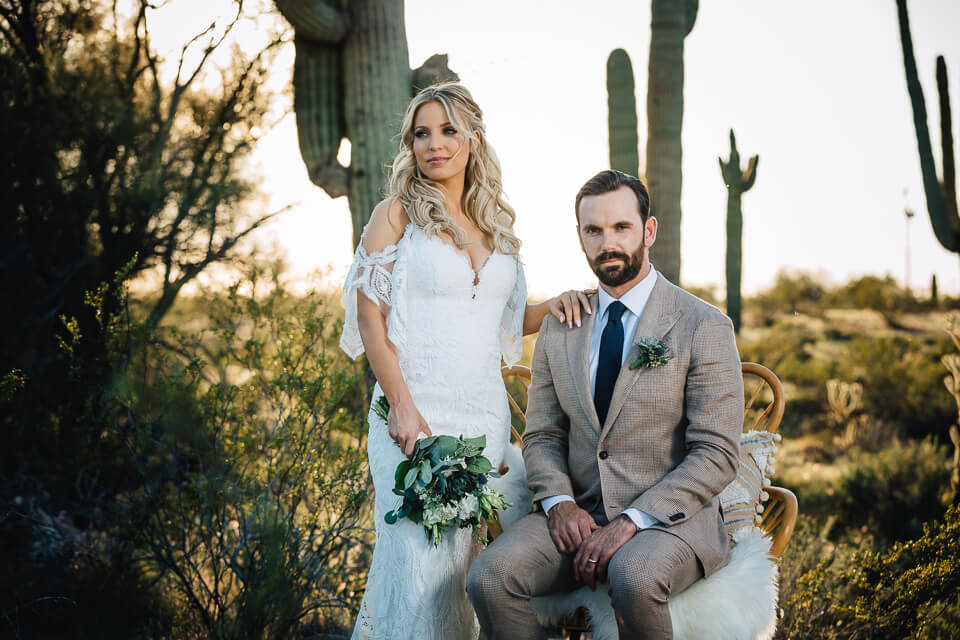 Bride and groom posing with a wicker chair in the desert for their Arizona elopement style wedding.