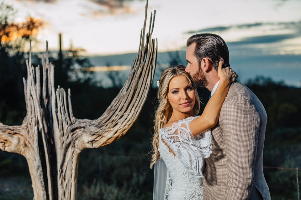 Bride embracing groom around the neck during a sunset for their Arizona elopement style wedding.