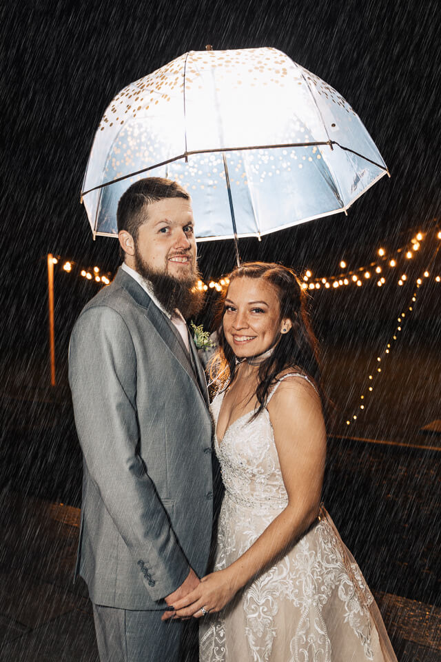 Bride and groom standing in the rain while holding an umbrella. 