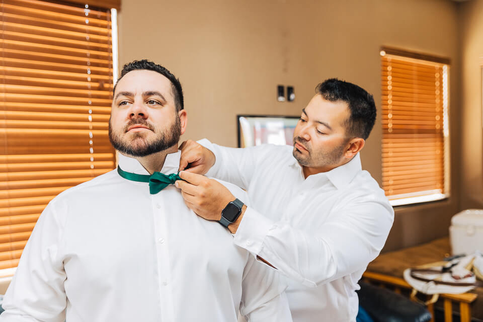 Groom getting help from his best man in getting ready. 