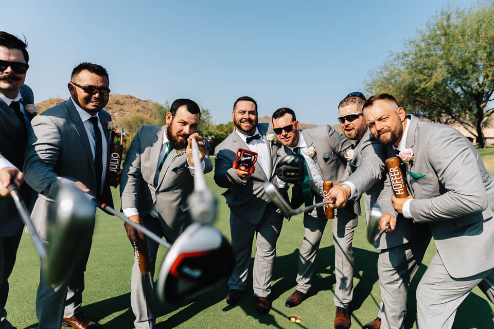 Groom and groomsmen holding golf clubs while standing on a green. 
