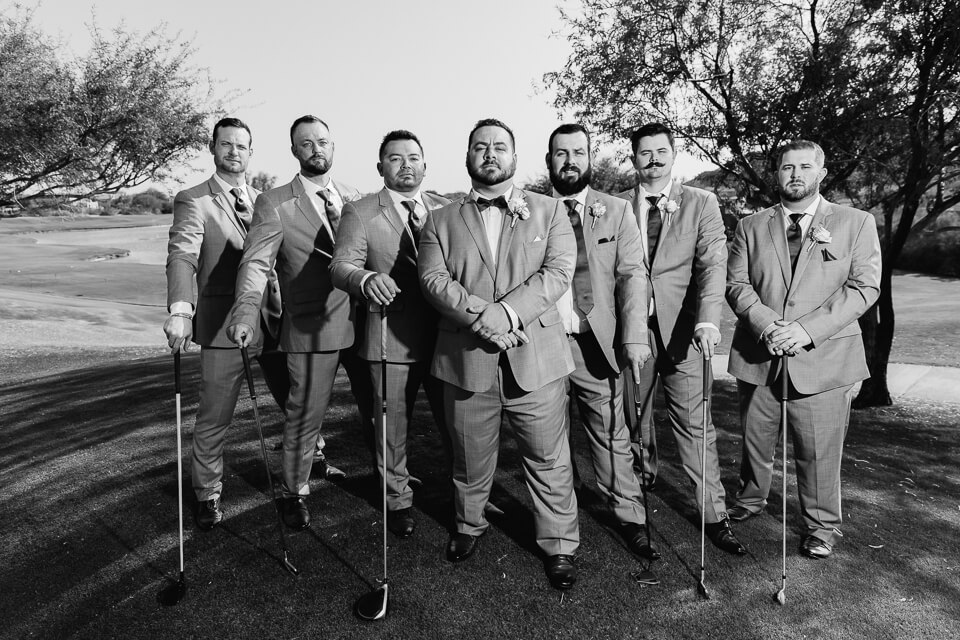 Groom and groomsmen posing with golf clubs. 