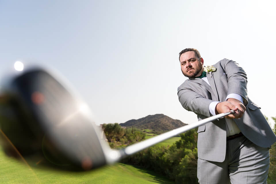 Groom swinging golf club at golf course wedding. 