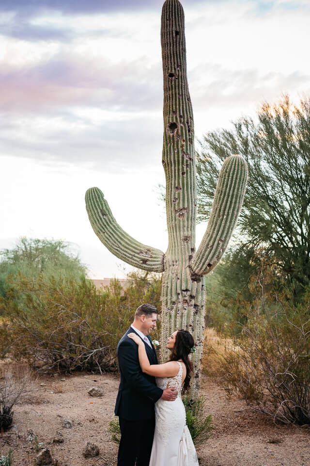 Bride and groom holding each other in front of a saguaro cactus.