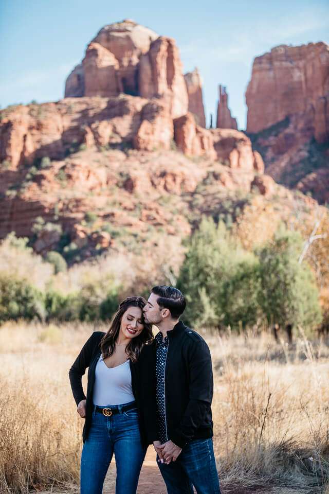 Engaged couple standing in front of Cathedral Rock at Red Rock Crossing. 