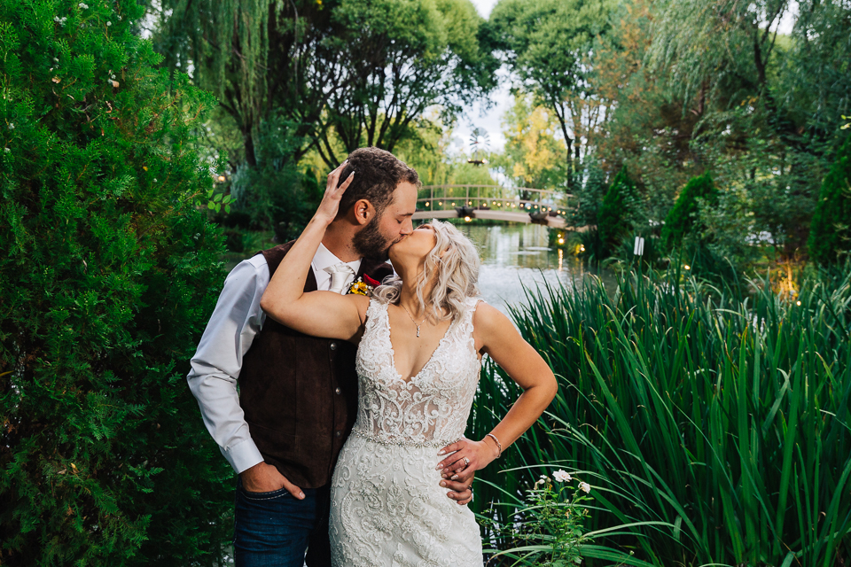 Bride and groom kissing by a small pond.