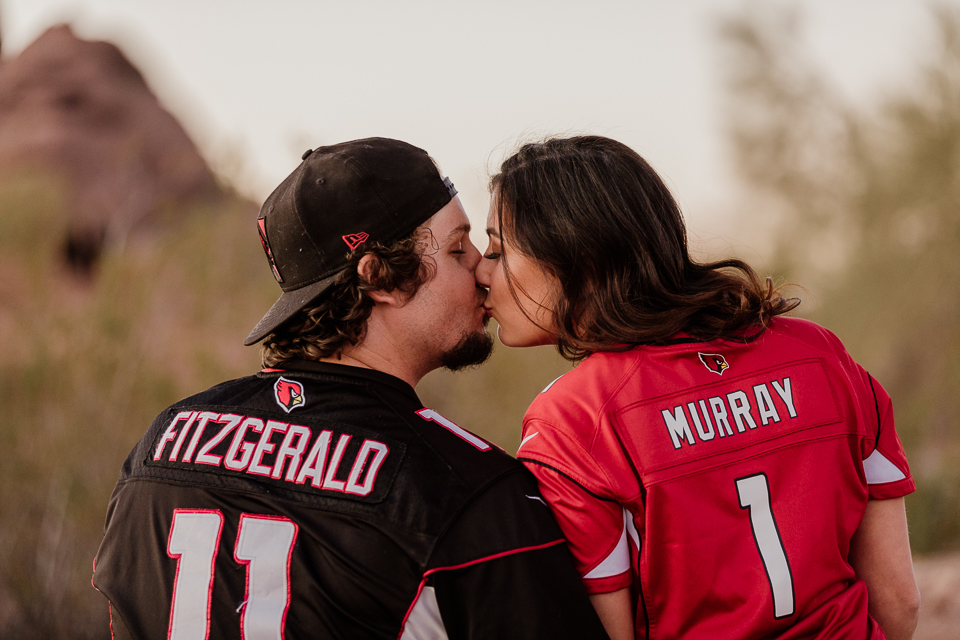 Couple wearing football jerseys while holding their dog.