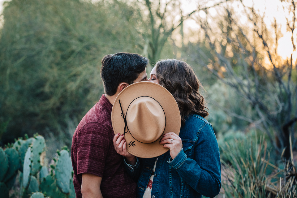 Couple kissing behind a hat.