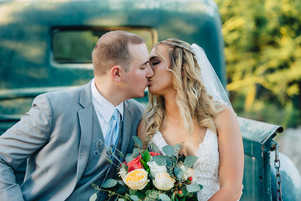 Bride and groom sitting on a green truck tailgate kissing.