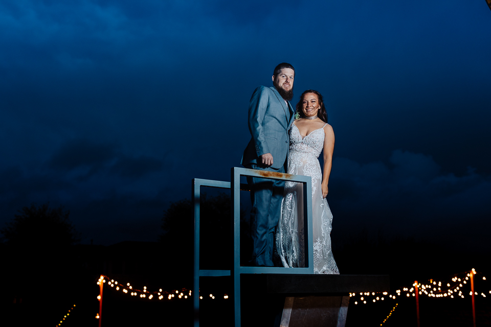 Bride and groom standing on a high dive above a swimming pool.