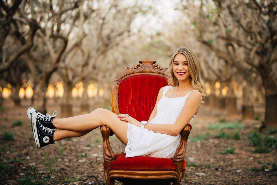 Senior girl wearing Converse sitting in a red Victorian chair.