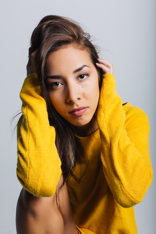 Model wearing a yellow sweater touching her face.